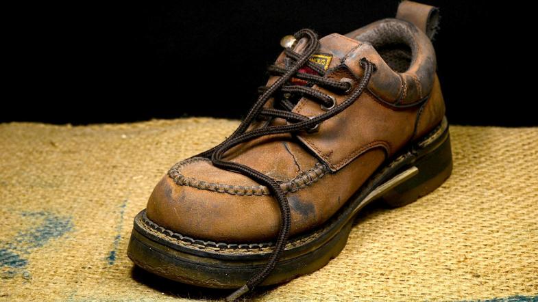 Ein brauner Lederschuh mit dicken Nähten steht auf einem gelben Tuch