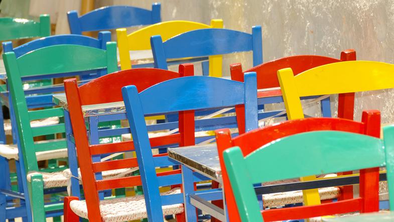 Holzstühle in verschiedenen Farben (grün, rot, blau und gelb) stehen aufgereiht hinter- und nebeneinander