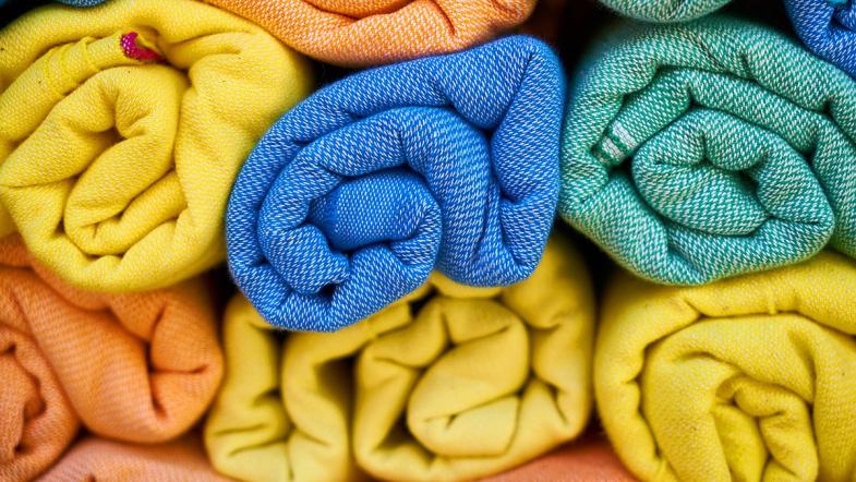 Stoffrollen neben- und aufeinander gestapelt in verschiedenen Farben (blau, orange, grün und gelb)