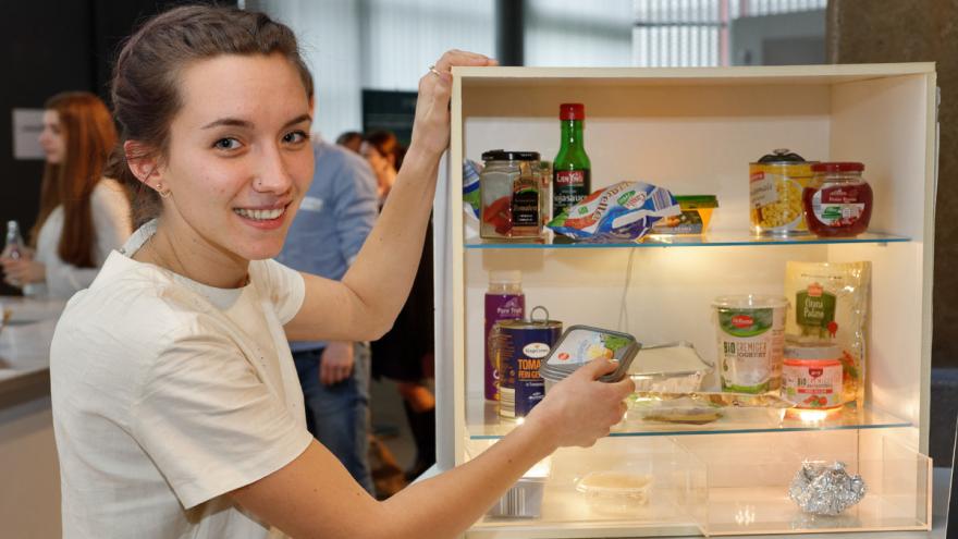 Studentin neben einem Regal, in dem beleuchtete Kühlschrankplatten eingebaut sind