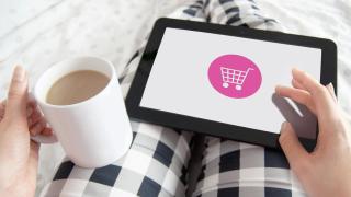 Tablet mit Einkaufswagen-Symbol auf Schoß mit karierter Schlafanzughose