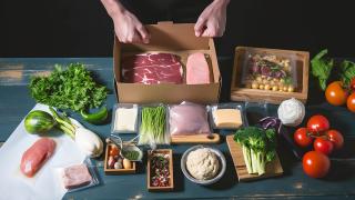 Diverse Lebensmittel werden in einem Pappkarton zusammengestellt.