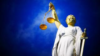 Statue der Justizia mit Waage und Schwert vor blauem Himmel