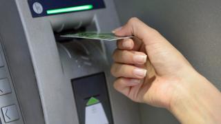 Eine Hand hält eine Karte vor den Schlitz eines Geldautomaten