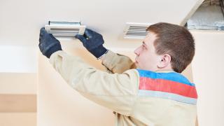 Installateur arbeitet an Lüftungsöffnung an einer Decke