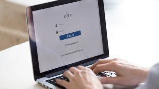 Zwei Hände auf einer Laptop-Tastatur, auf dem Bildschirm sind Eingabefelder zum Einloggen in ein Online-Konto zu sehen.