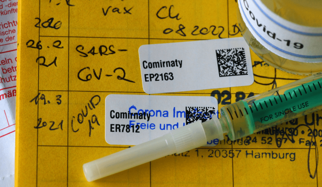 Ein Impfausweis, in dem zwei Impfungen gegen Corona eingetragen sind. Darauf liegt eine Spritze.