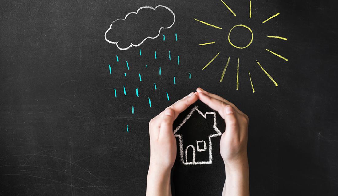 Hand schützt geszeichnetes Haus vor gezeichneten Regen und Sonnenstrahlen