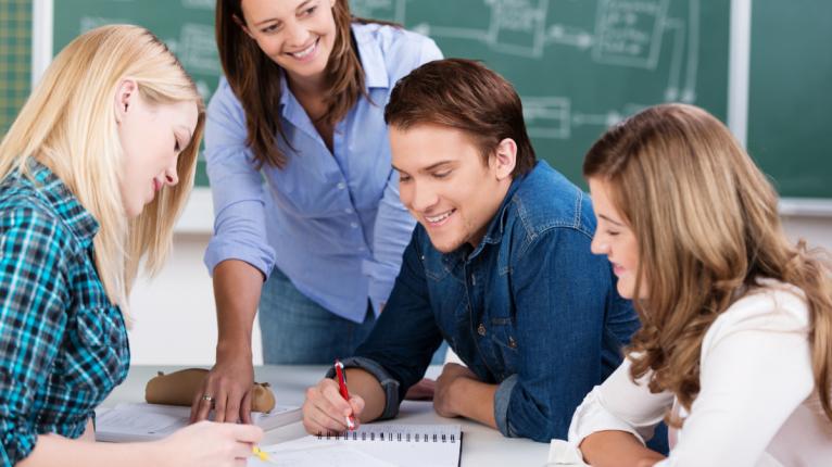 Drei Schüler arbeiten in der Gruppe, ihre Lehrerin steht mit am Tisch.