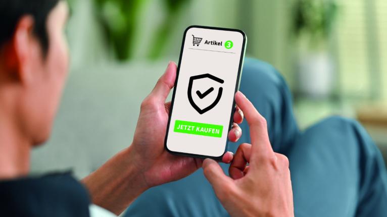 Ein Mann hält auf einem Sofa liegend ein Smartphone in der Hand, auf dessen Display ein Einkaufswagen und ein Schild zu sehen sind sowie die Aufschrift: "3 Artikel jetzt kaufen"