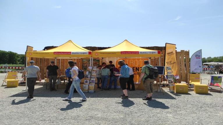 Aktionsstand mit gelben Sonnenschirmen, davor stehen mehrere Personen