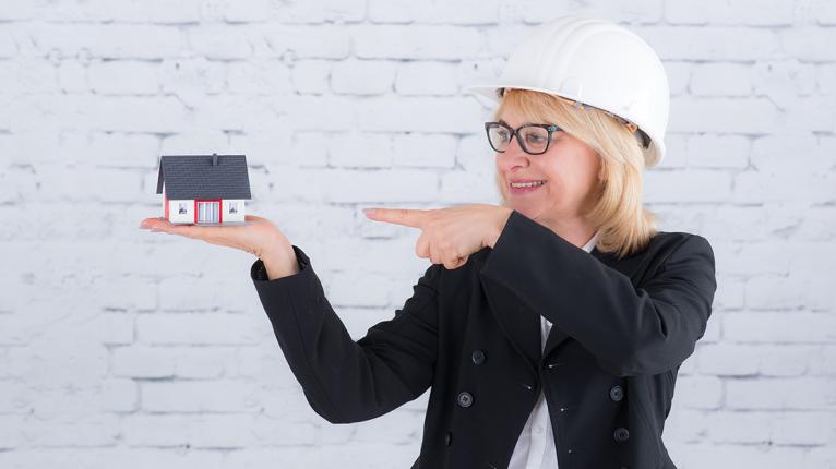 Frau mit Bauhelm zeigt auf Modellhaus auf Hand